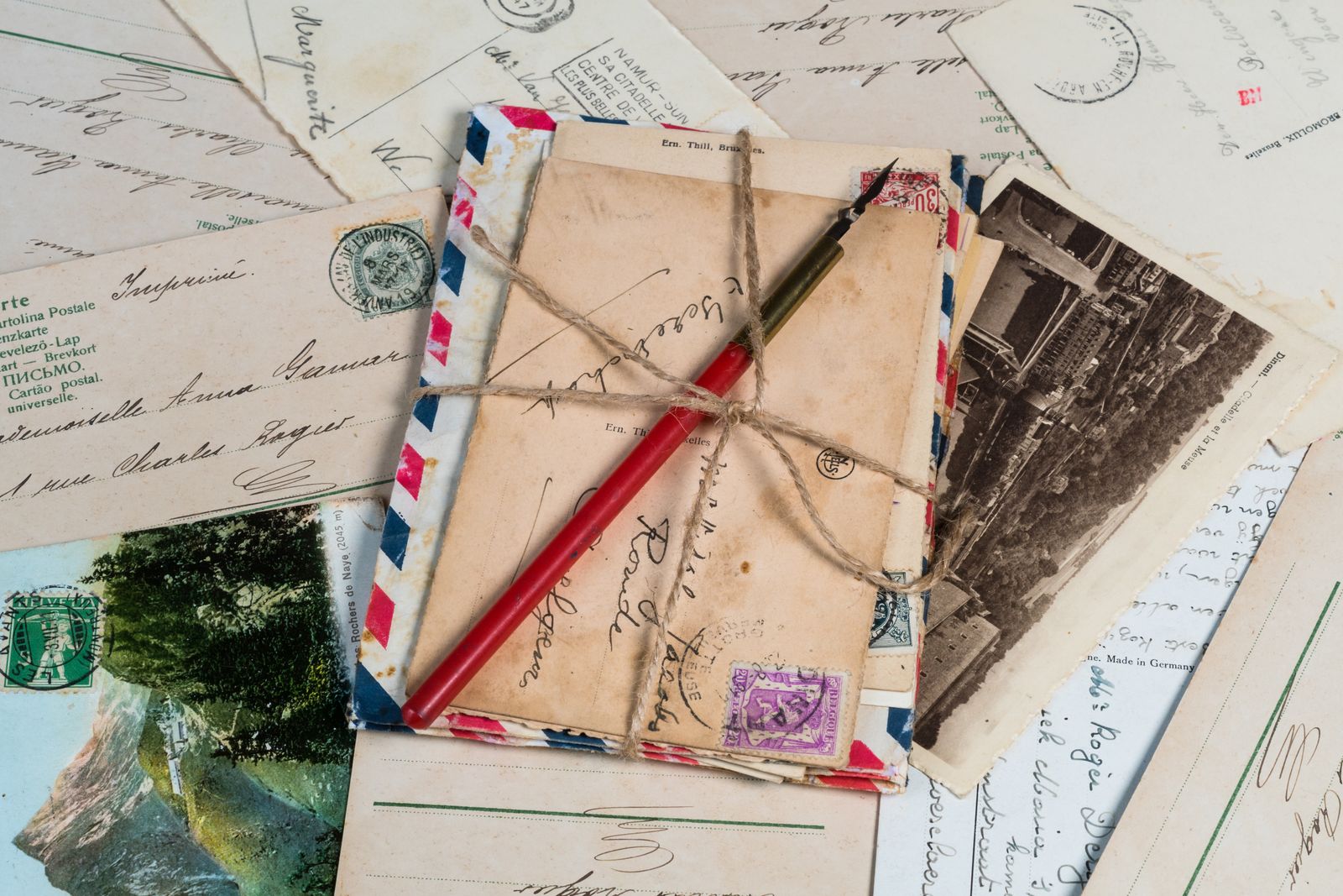 Vintage envelopes and postcards tied with twine beside a fountain pen